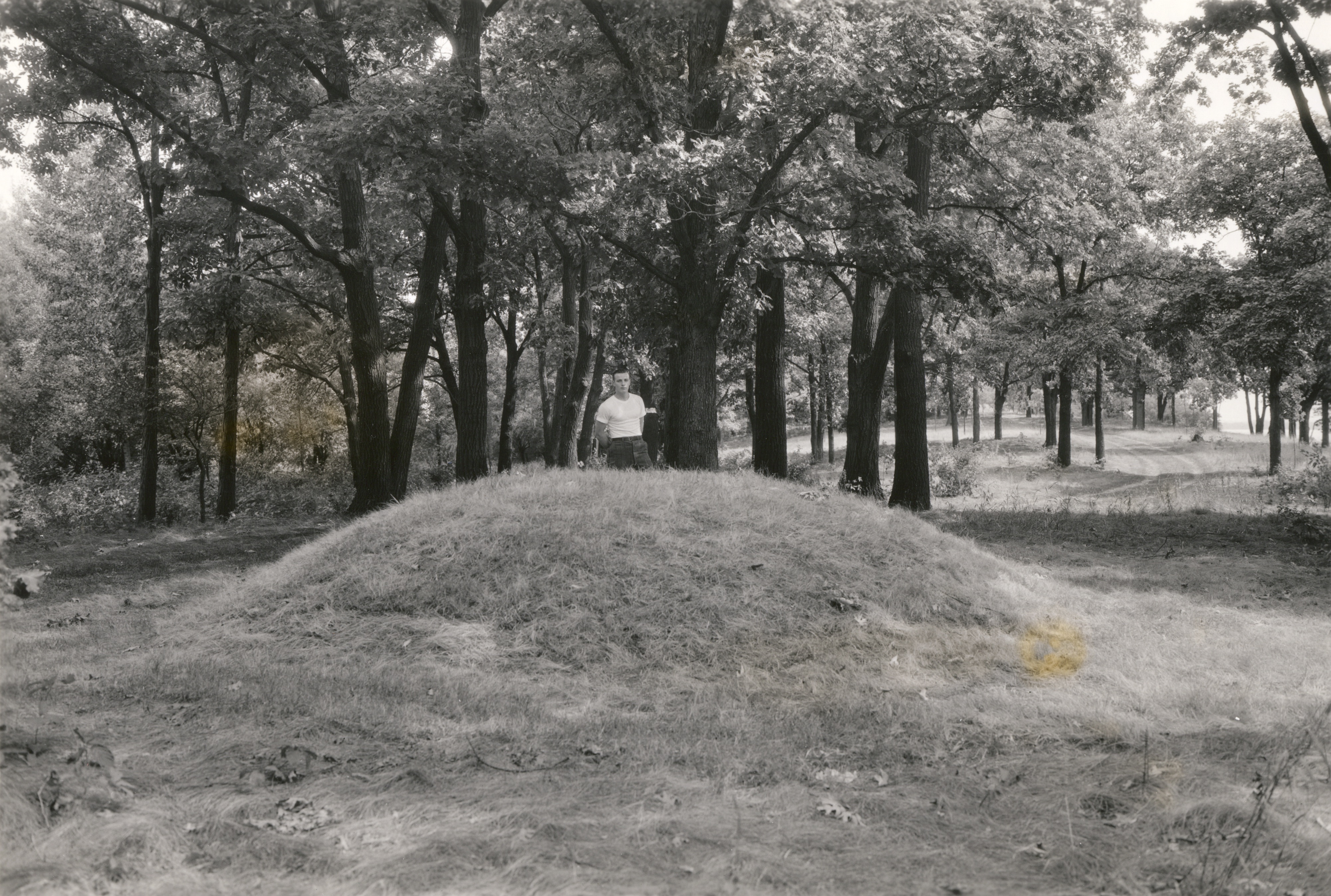 A man poses behind a conical Native American burial mound near the west end of Picnic Point on the University of Wisconsin-Madison campus.